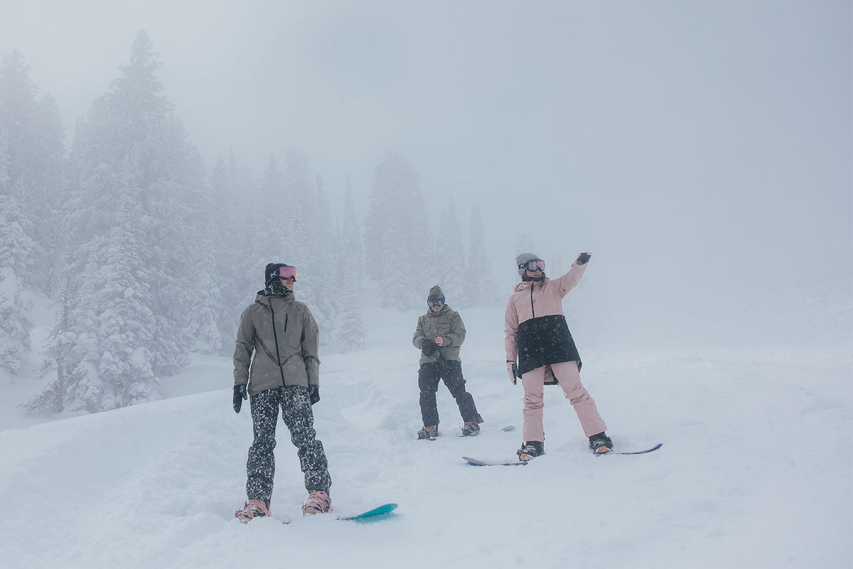Burton DRYRIDE: A group of three snowboarders on a powder-covered ski trail with snow falling, deciding where to ride.