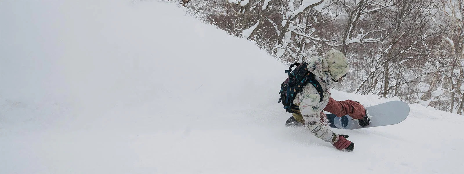 A person snowboarding down a snowy hill with trees in the background.