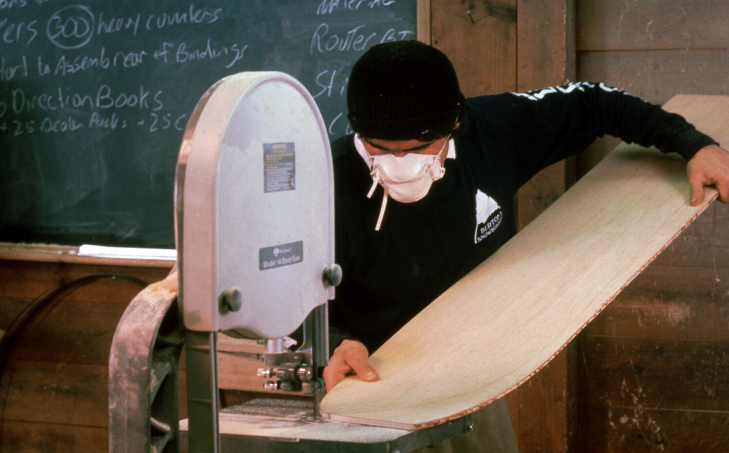 Person using a bandsaw to cut a piece of wood in a workshop setting.