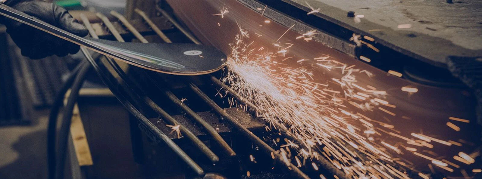 Person using a grinder to sharpen the edges of a snowboard with sparks flying