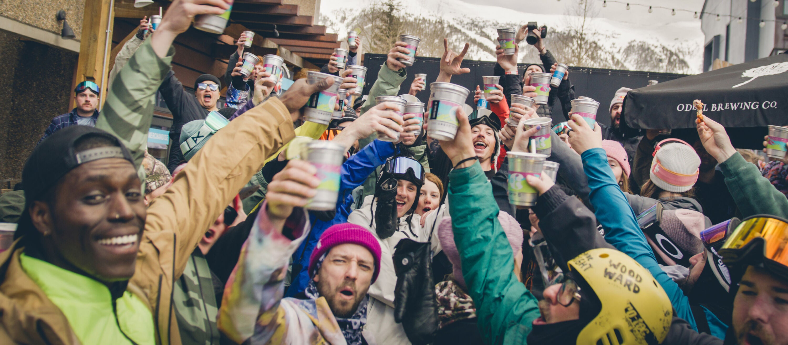 Group of people raising their hands with cans in a celebratory manner outdoors.