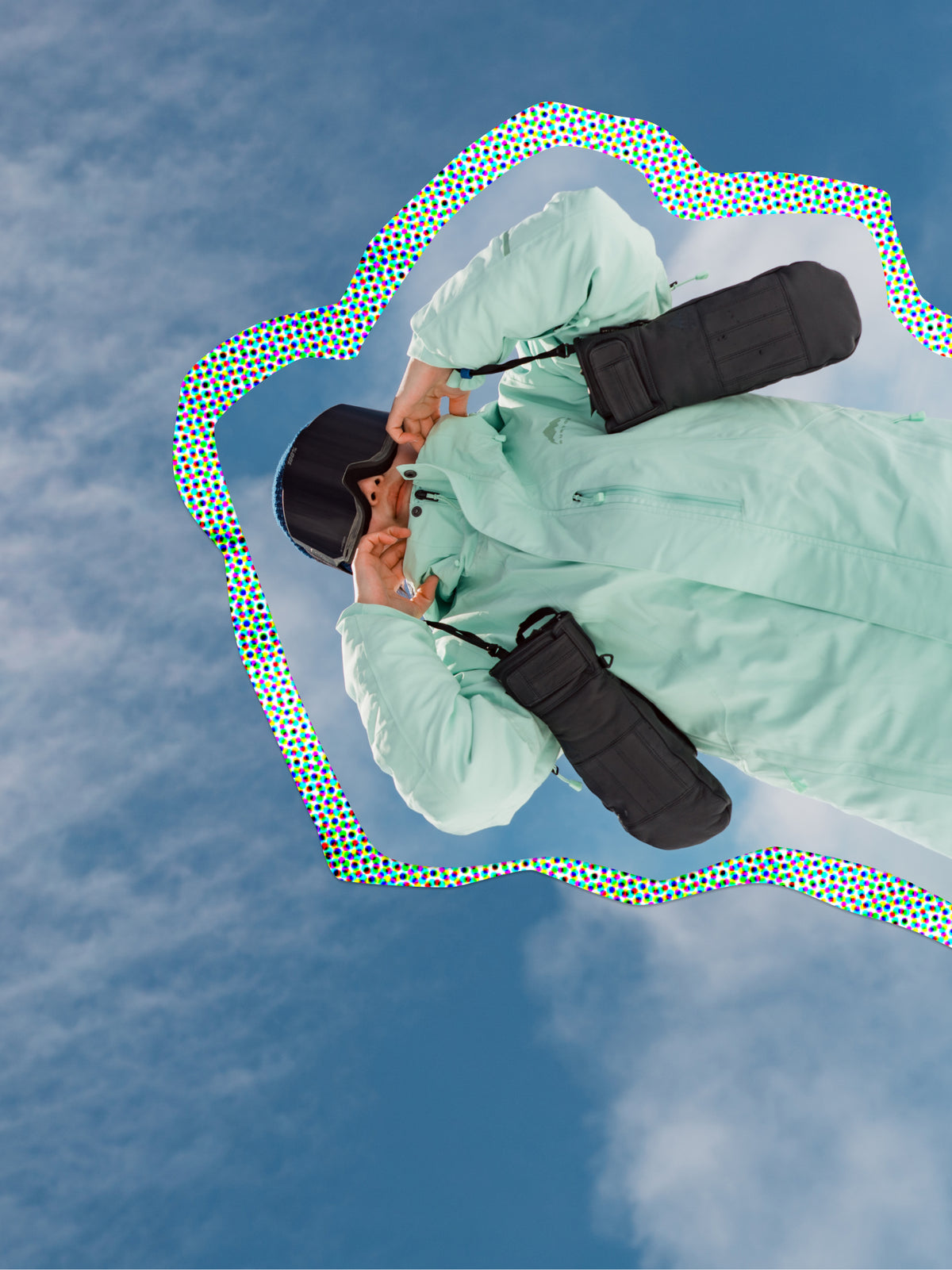 snowboarder holding gloves in front of a cloudy, blue sky