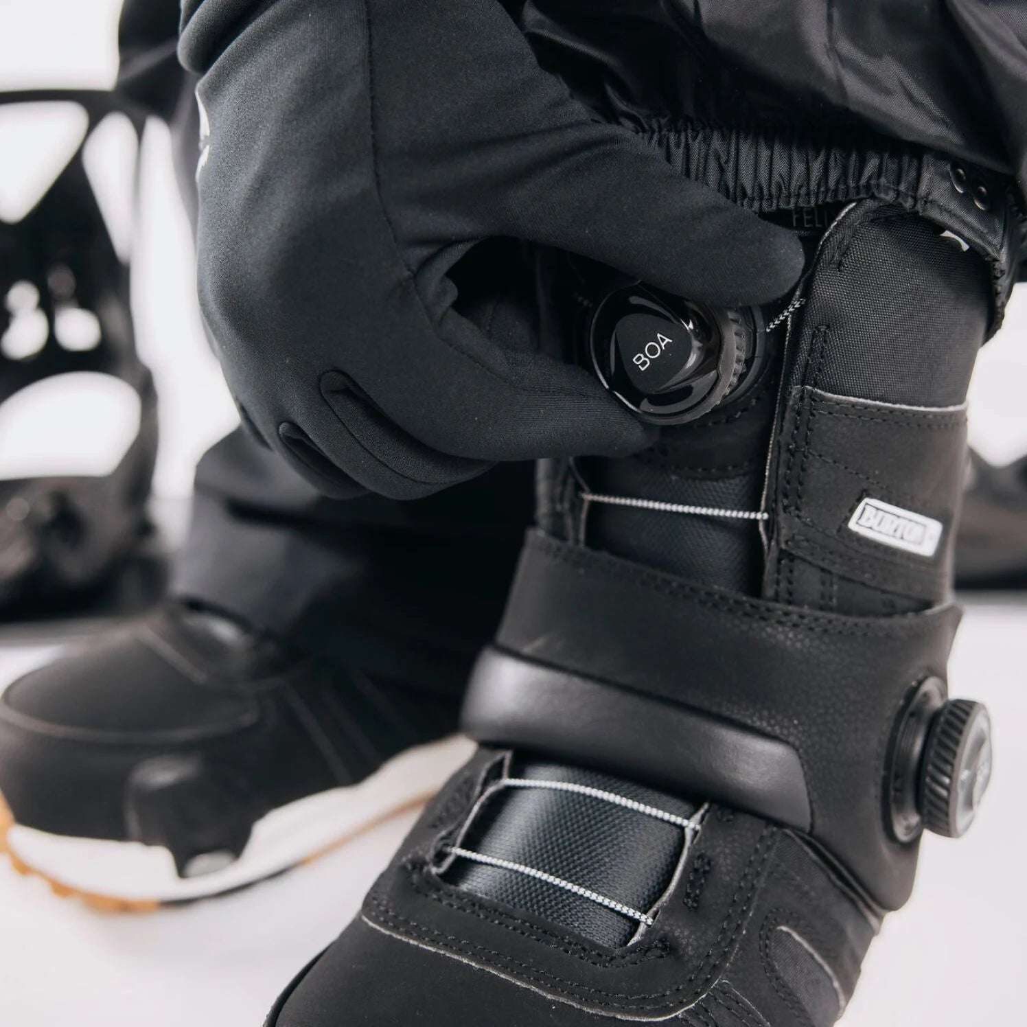 Person adjusting BOA system on a black snowboard boot with a white background