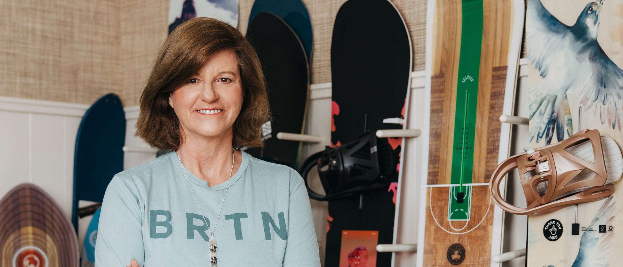 A photo of Donna Carpenter standing in front of snowboards leaning against the wall behind her.