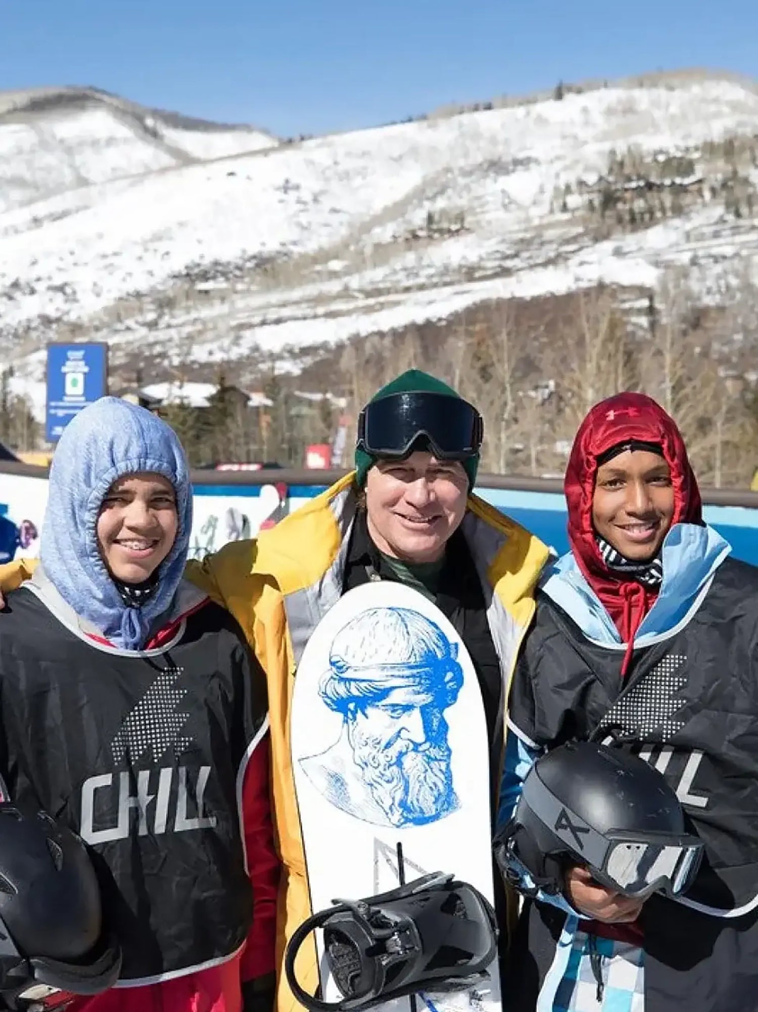Three snowboarders posing with a snowboard in a snowy mountainous area
