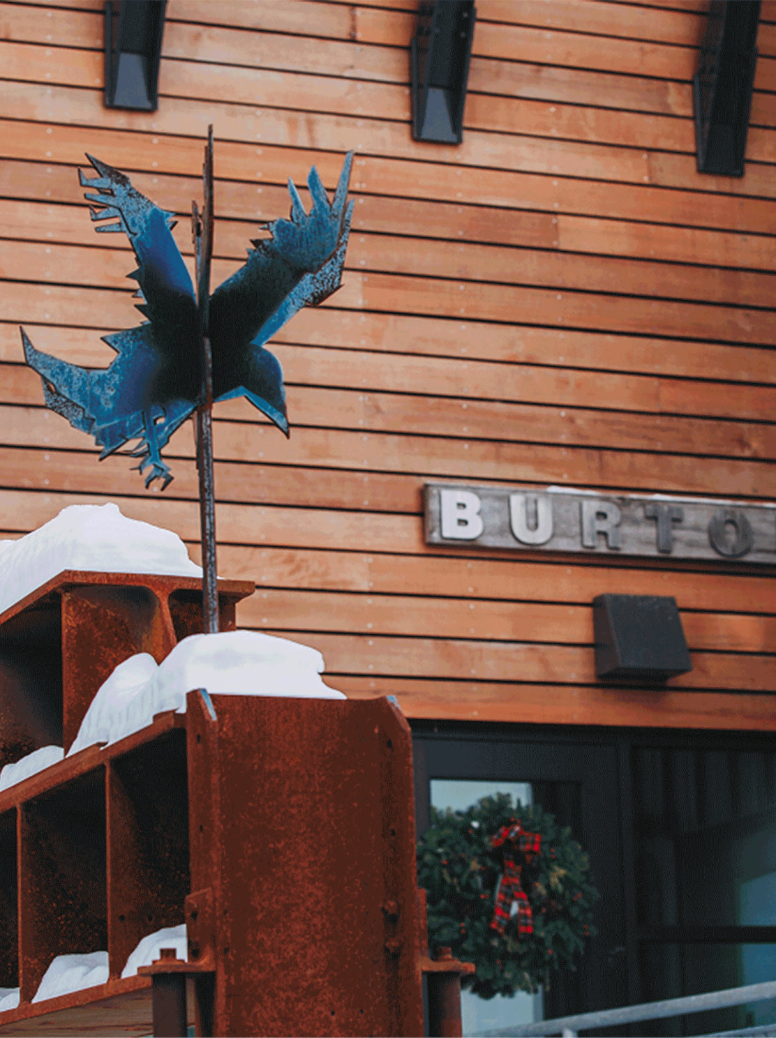 photo of wood sided building with a metal sculpture of a bird in front. sign reads "burton"