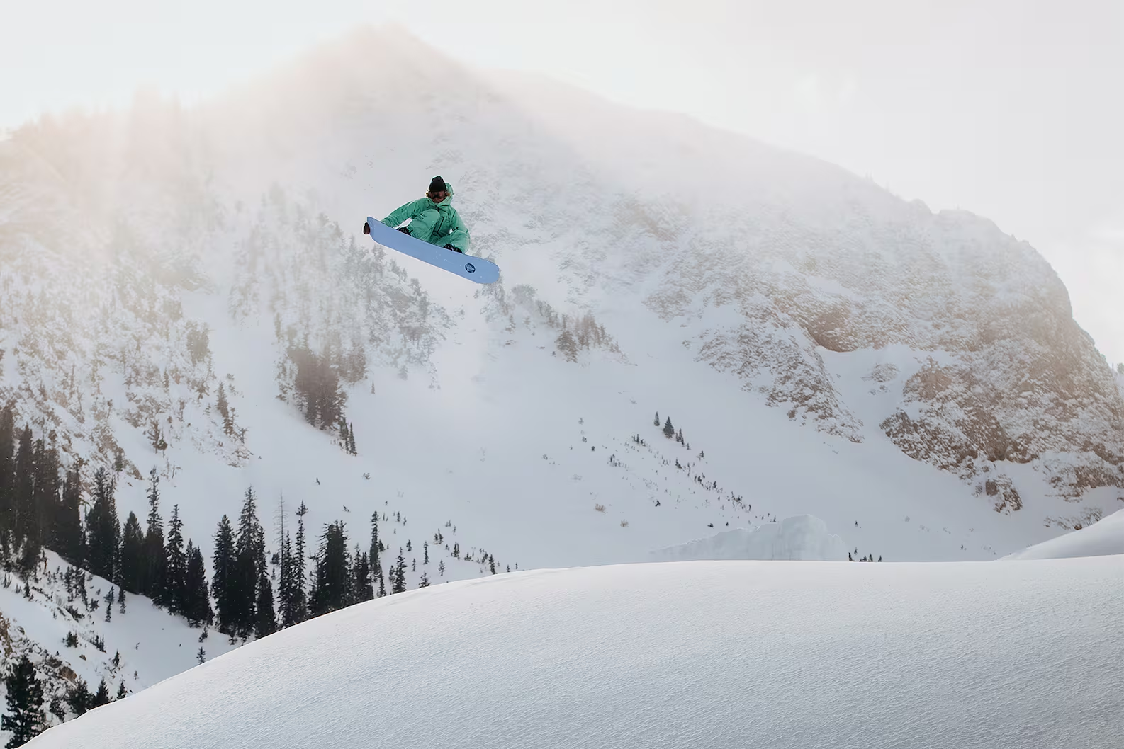 Person snowboarding down a snowy mountain with trees in the background