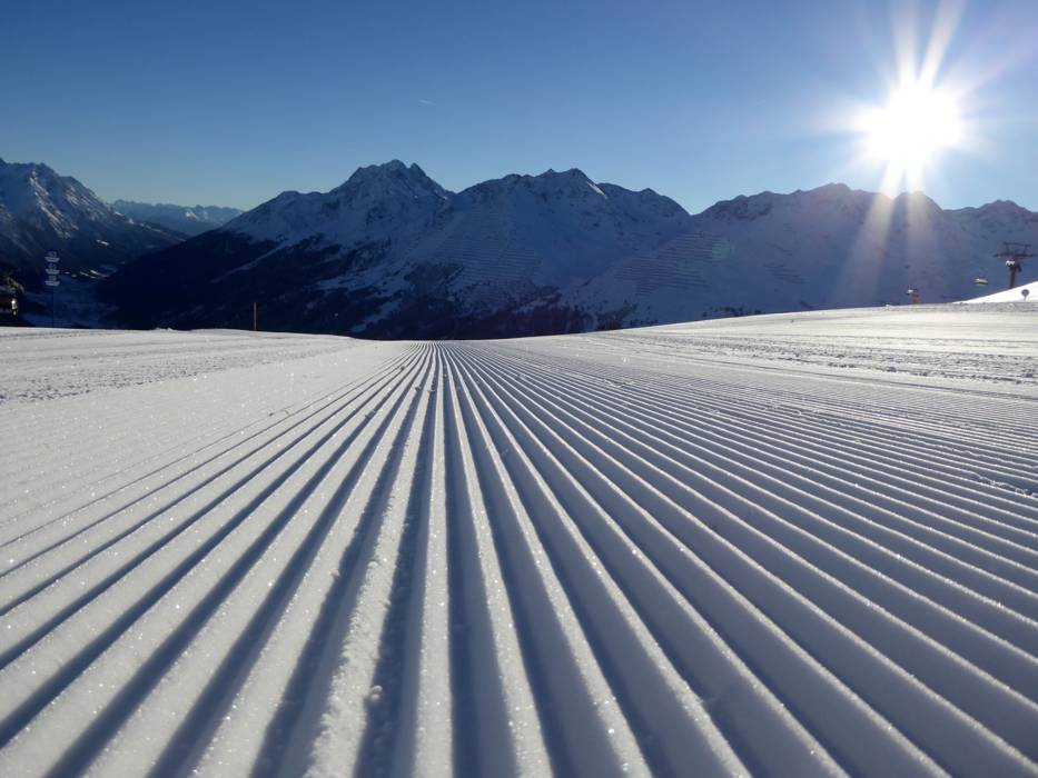 Snow-covered slope with mountains in the background under a clear blue sky.